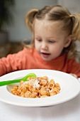 Small girl with pasta with tomato sauce and Parmesan