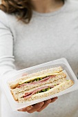 Woman holding two salami & cheese sandwiches in packaging