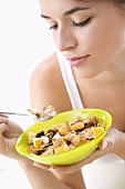 Young woman eating cornflakes with fruit and yoghurt