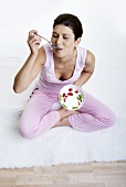 Frau isst genussvoll Joghurt mit Kiwi und Erdbeeren