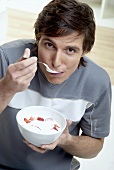 Young man eating quark with fresh strawberries