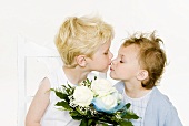 Two children kissing over a bouquet of white roses