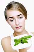 Young woman holding a plate of fresh basil leaves