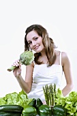 Young woman holding an artichoke, green vegetables in front