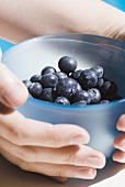 Hands holding blueberries in small blue bowl