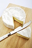 Camembert with a piece cut out on a wooden board with knife