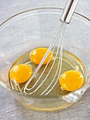 Three eggs broken into a glass bowl with whisk