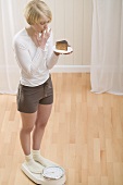 Young woman with a piece of cake on scales