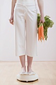 Young woman with carrots on bathroom scales