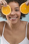 Young woman holding orange slices in front of her face