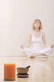 Young woman meditating, candle and singing bowl