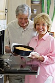 Couple baking cake standing next to oven