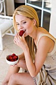 Blond woman, seated, eating strawberry