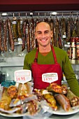 Shop assistant with various sausages in butcher's shop