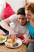 Couple eating fruit, chocolate and rusks in living room