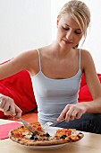 Woman eating pizza with knife and fork in living room