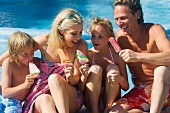 Family eating ice-cream next to pool on holiday