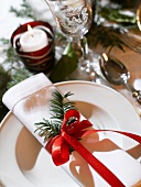 Place-setting with fabric napkin, fir sprig and red bow