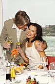 Couple with wine glasses at laid table by sea