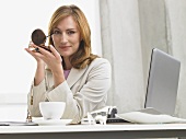 Businesswoman putting on eye make-up at her desk
