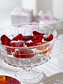Red flower petals and floating candles in glass bowl