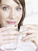Woman holding glass of water and tablets