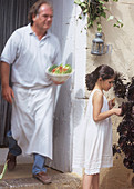 Koch serviert Salat vors Haus, Mädchen neben Kübelpflanze