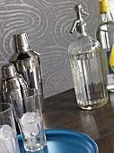 Cocktail shaker, glasses with ice cubes, soda syphon