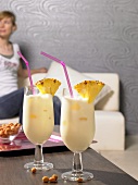 Two pina coladas on table, woman on sofa in background