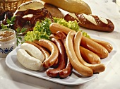 Mixed sausages on a platter, bread rolls and mustard behind