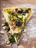 Two pieces of pizza with mince, olives, spinach and cheese