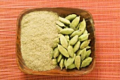 Cardamom pods and ground cardamom in wooden bowl