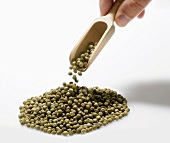 Hand dropping green peppercorns from wooden scoop