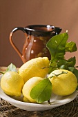Fresh lemons with leaves on plate in front of terracotta jug