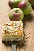 Piece of apple crumble cake, fresh apples in background