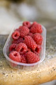 Raspberries in plastic punnet on a stone sink