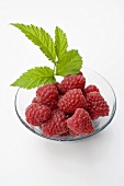 Several raspberries with leaves in glass bowl