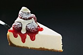 Slice of cheesecake with raspberries, cream, icing sugar on server