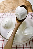 Mozzarella with brine in glass bowl and on wooden spoon