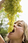 Woman holding fresh green grapes above her mouth