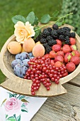 Plums, apricots and berries in wooden bowl
