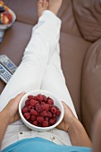 Woman watching TV holding bowl of fresh raspberries