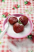 Three strawberries in a small dish of sugar