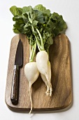 Icicle radishes with leaves & knife on chopping board