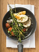 Sea bass cutlets with vegetables, herbs, lemon in frying pan