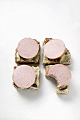 Four open sausage sandwiches with mustard, one with bite taken