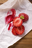 Strawberry jam on spoon and fresh strawberries on paper