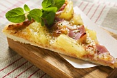 Stück Pizza Hawaii mit frischem Oregano auf Schneidebrett