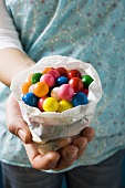 Hands holding coloured bubble gum balls in paper bag