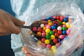 Hand taking bubble gum balls out of plastic bag with scoop